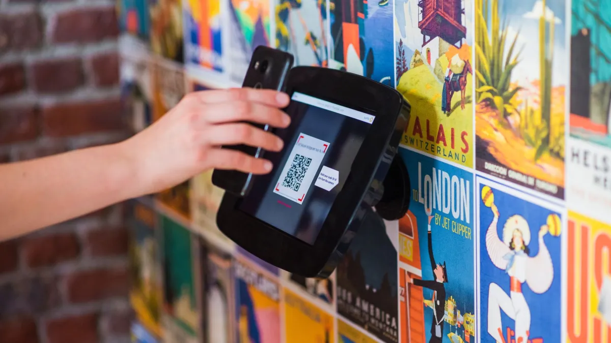 A hand scanning a QR code with a smartphone on a wall covered in vibrant posters indoors.