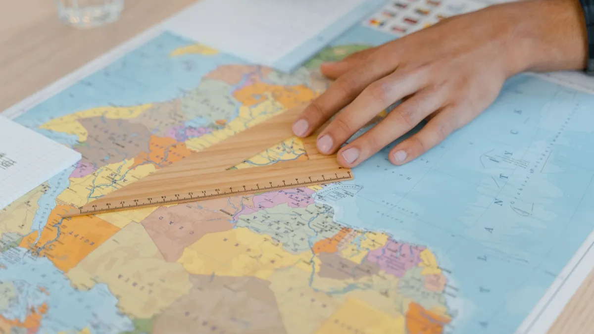 A hand uses a wooden ruler on a world map, focusing on precise measuring.